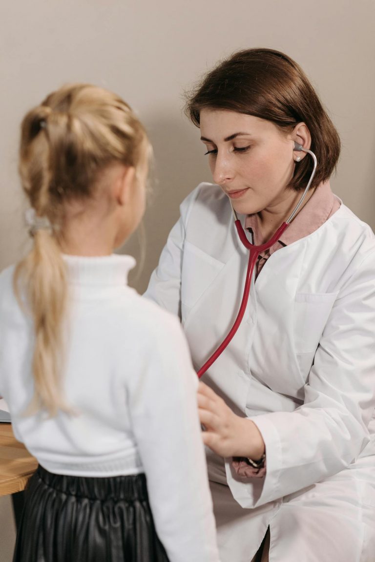 A female doctor examining a child with a stethoscope during a pediatric check-up in a clinic.