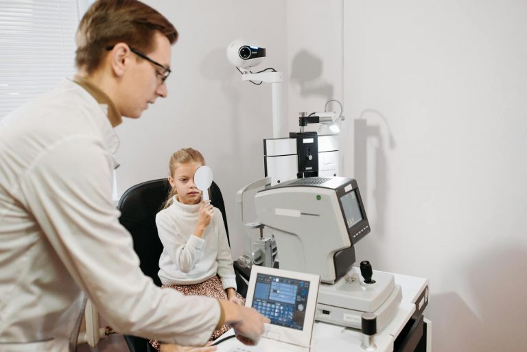 An optometrist using equipment to test a young girl's vision in a modern clinic setting.
